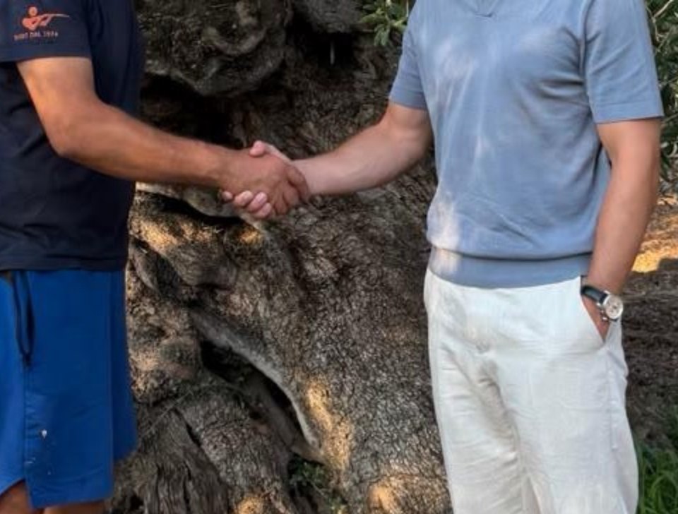 Maurice en de olijfboer geven elkaar een hand bij de stam van een oude olijfboom in de boomgaard bij Taranto